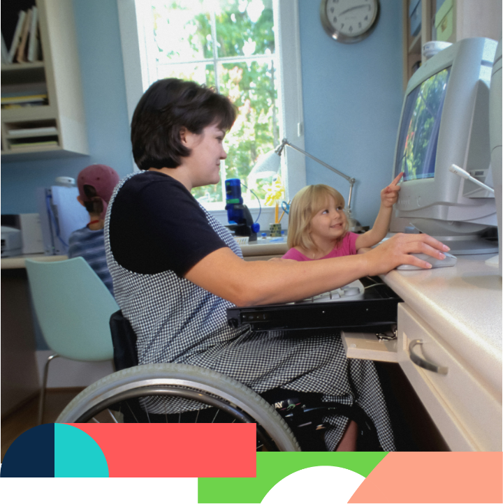 A person in a wheelchair using a desktop computer with a child